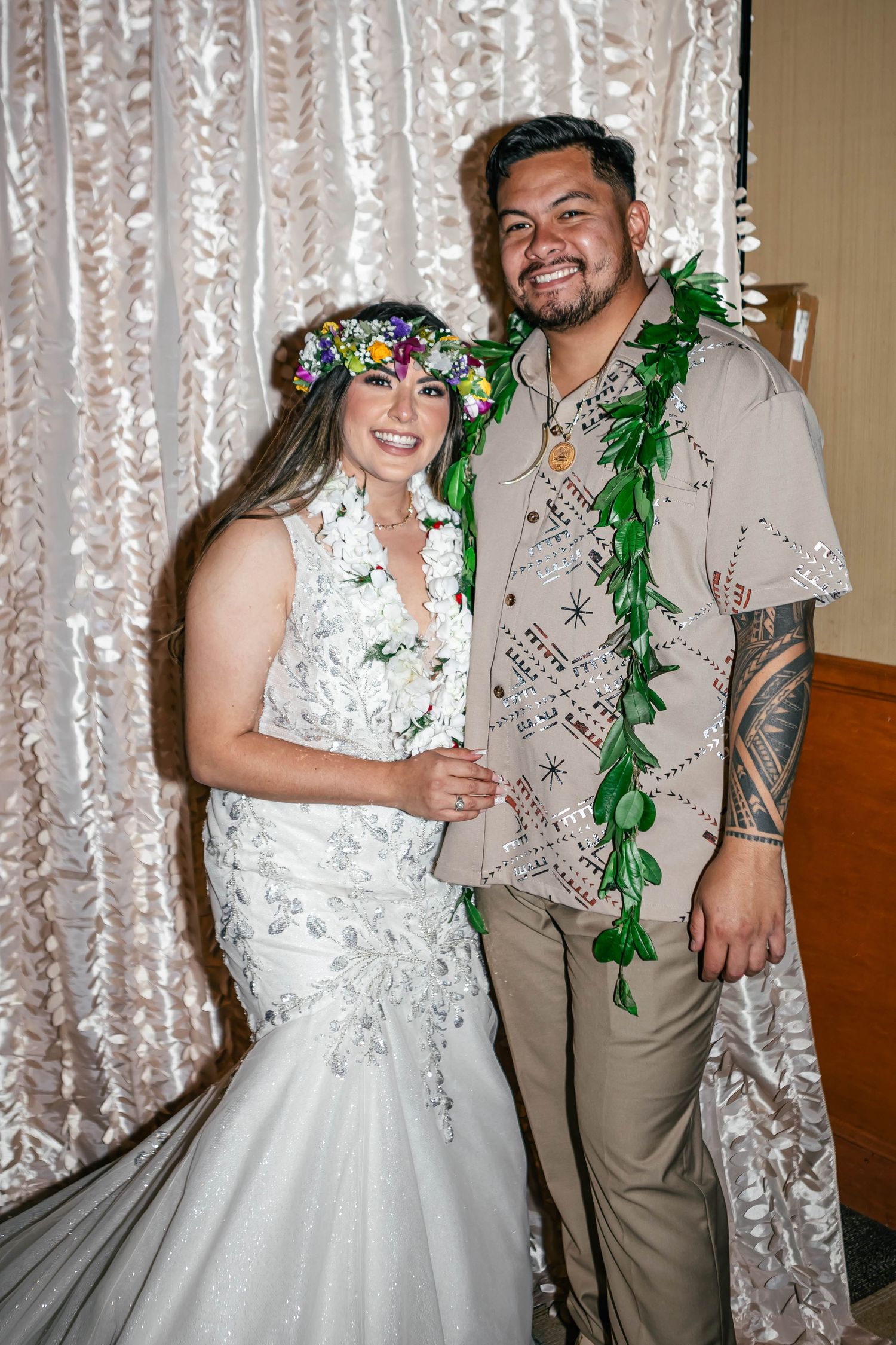 Wedding couple posing in front of sparkly curtain backdrop with green floral accents.