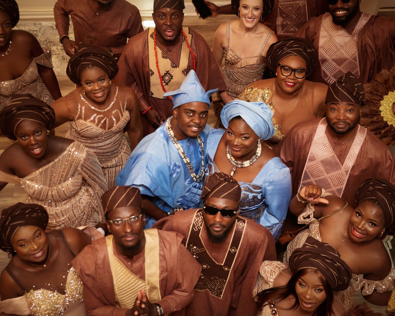 Large celebration group photo with guests in traditional African attire in brown and blue tones.