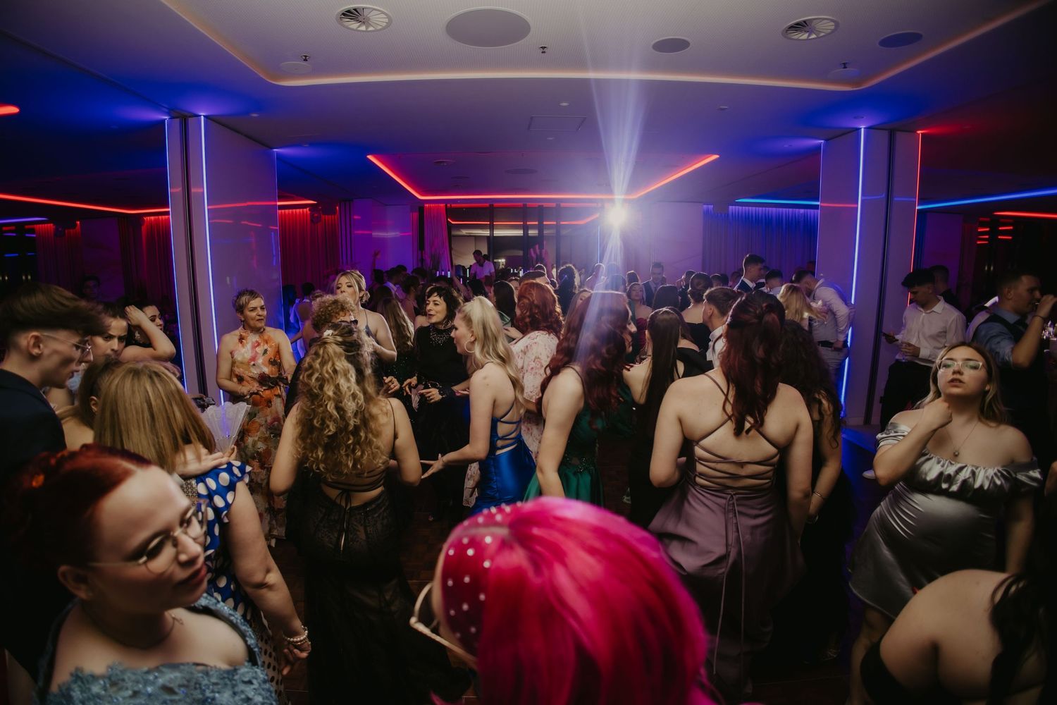 A crowded nightclub dance floor illuminated by blue and red lights with people dancing and socializing.