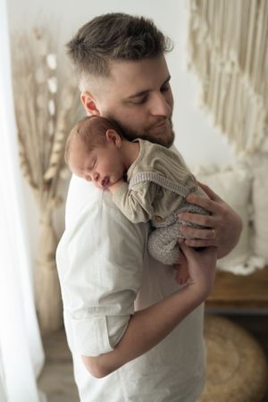 Giovane papà tiene sulla spalla il suo bimbo di pochi giorni che dorme pacifico