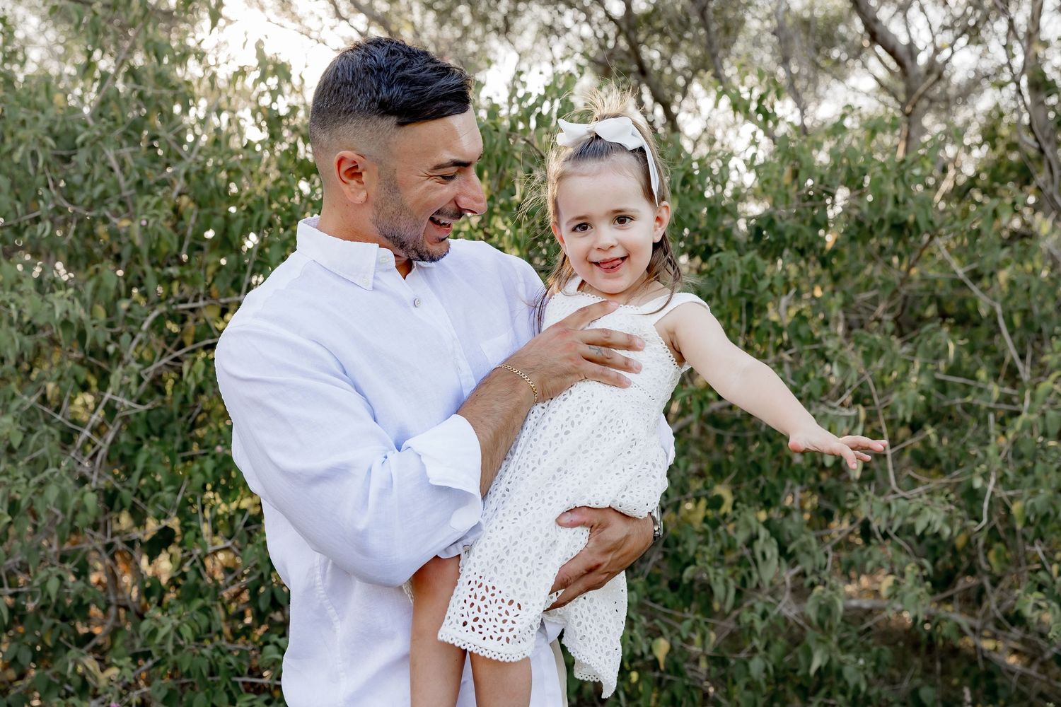 A joyful outdoor family photoshoot showing loving interactions in coordinated white outfits.