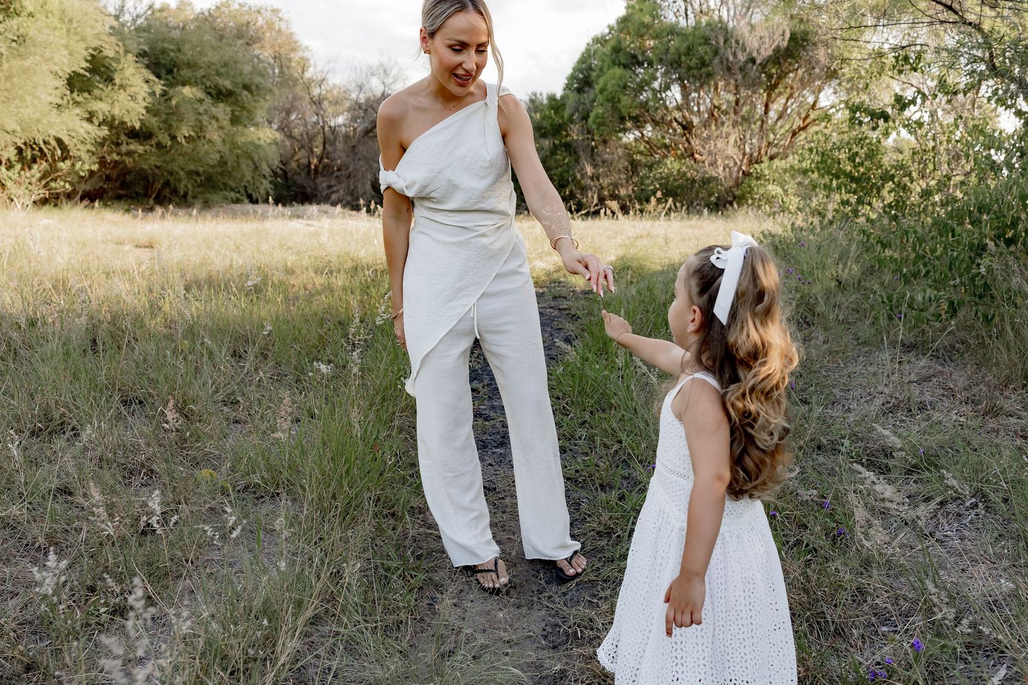 Two figures in white outfits are captured in a candid moment amid tall grasses.