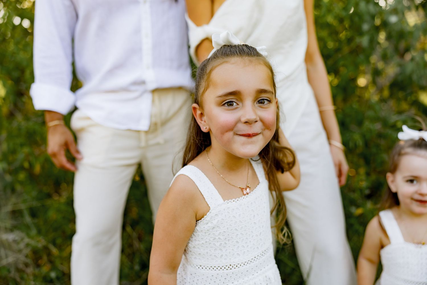 A wedding couple and bridesmaid pose in a garden setting wearing white with natural greenery.