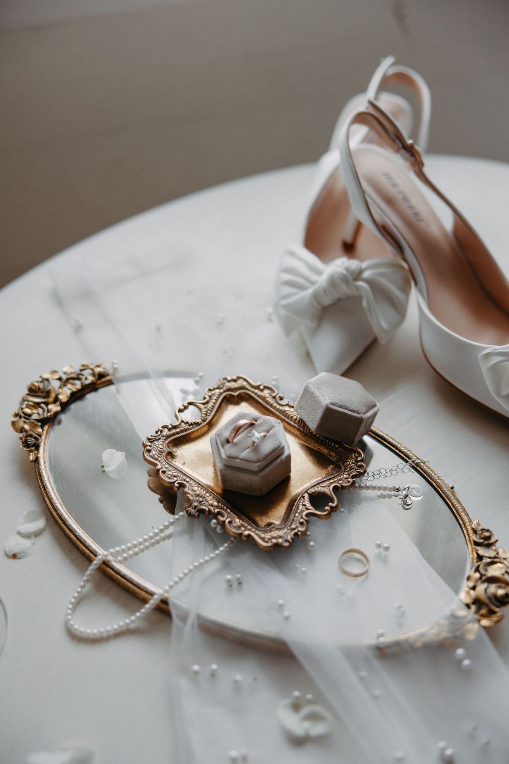 Wedding accessories including white bow heels and rings displayed on ornate gold tray with pearls.