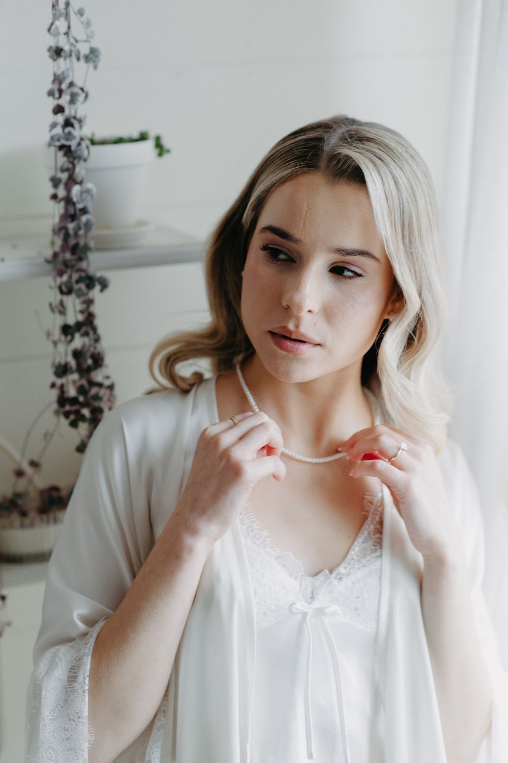 A person wearing a delicate white silk robe gazes softly in an elegant boudoir setting with floral decor.