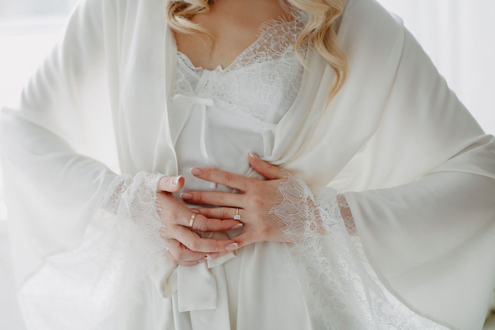 Close-up of delicate white lace and silk details on a wedding dress with hands clasped.