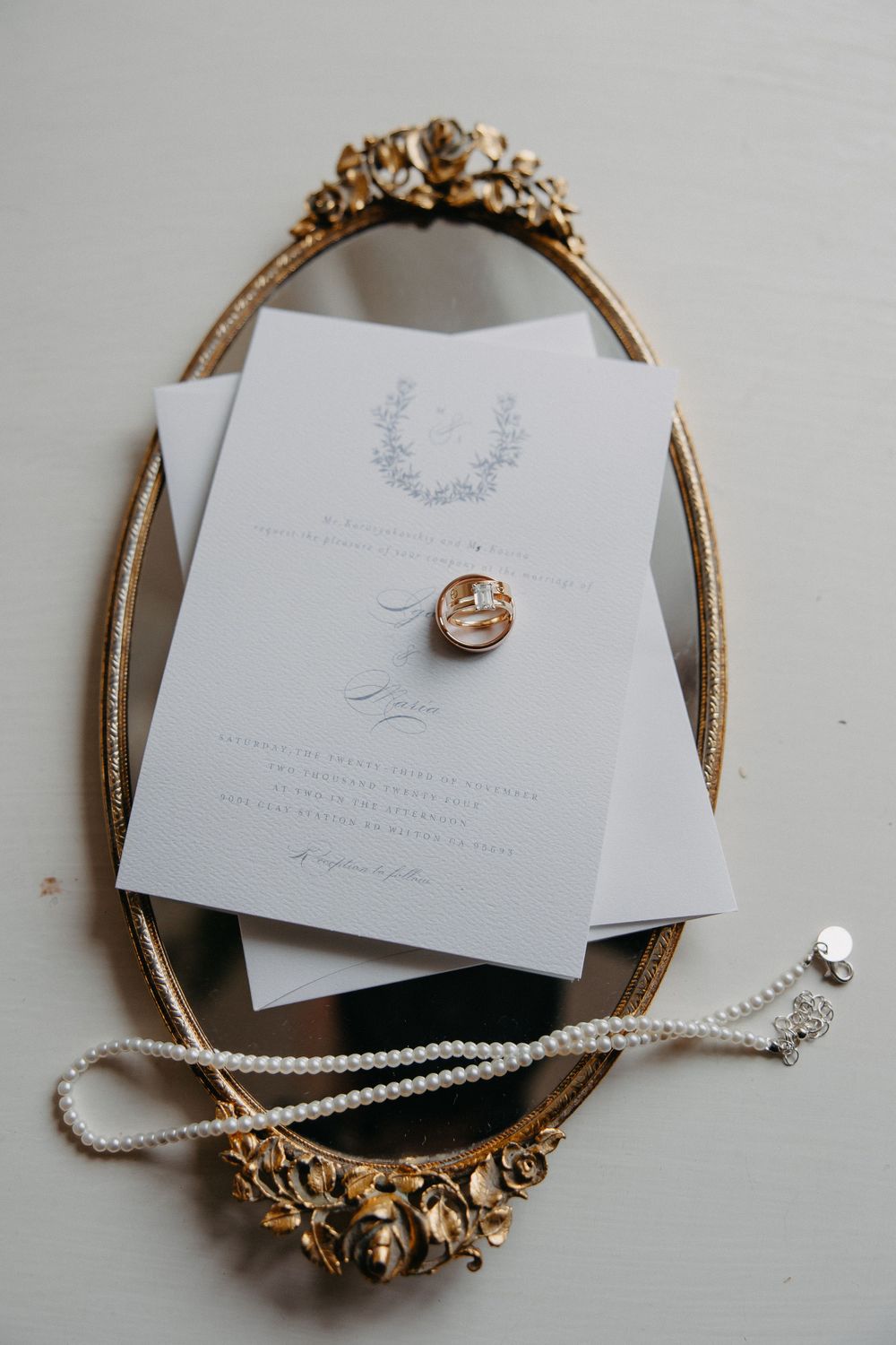 Wedding invitation and rings displayed on an ornate gold vintage mirror tray with delicate details.