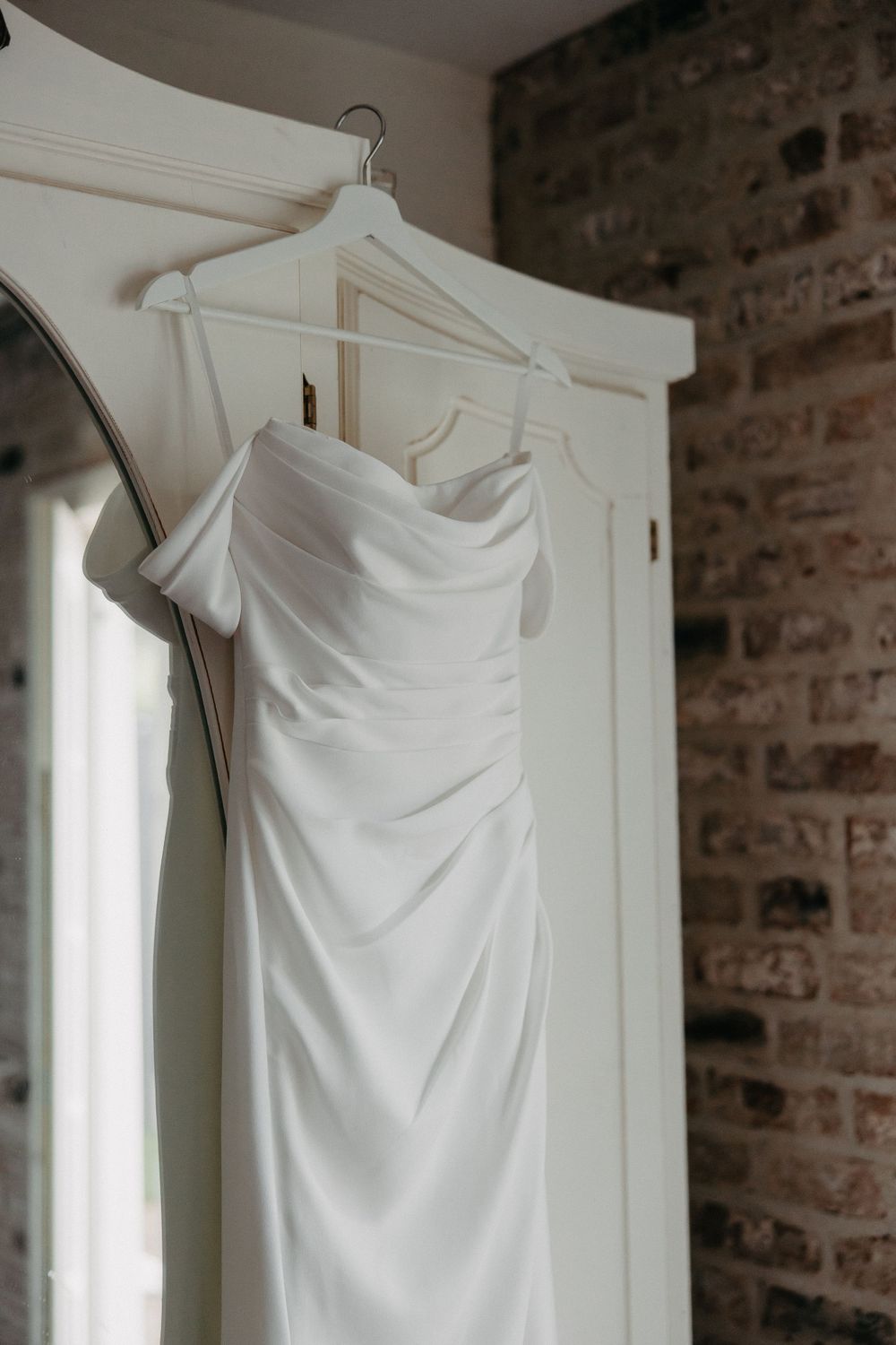 Elegant white wedding dress hanging on display against exposed brick wall.
