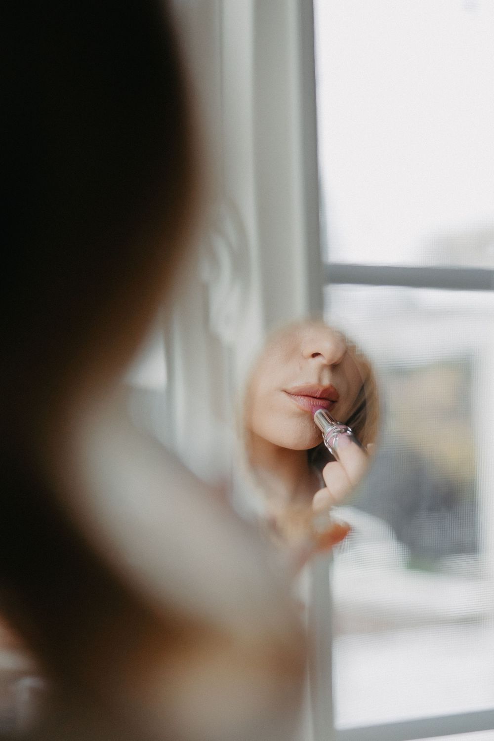Artistic soft focus reflection shot of makeup application in window light.