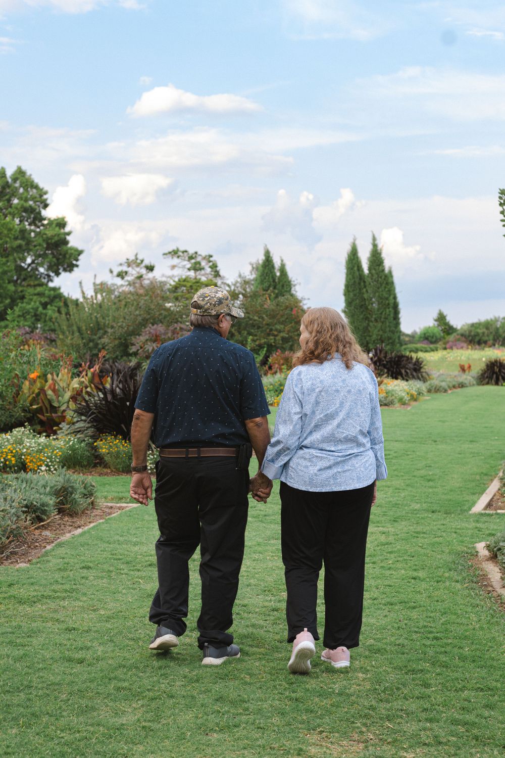 Couple takes a romantic stroll together on a grass path through a landscaped garden.