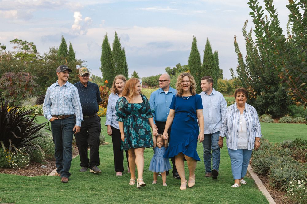 Family group walking together through a garden setting with cypress trees in background.