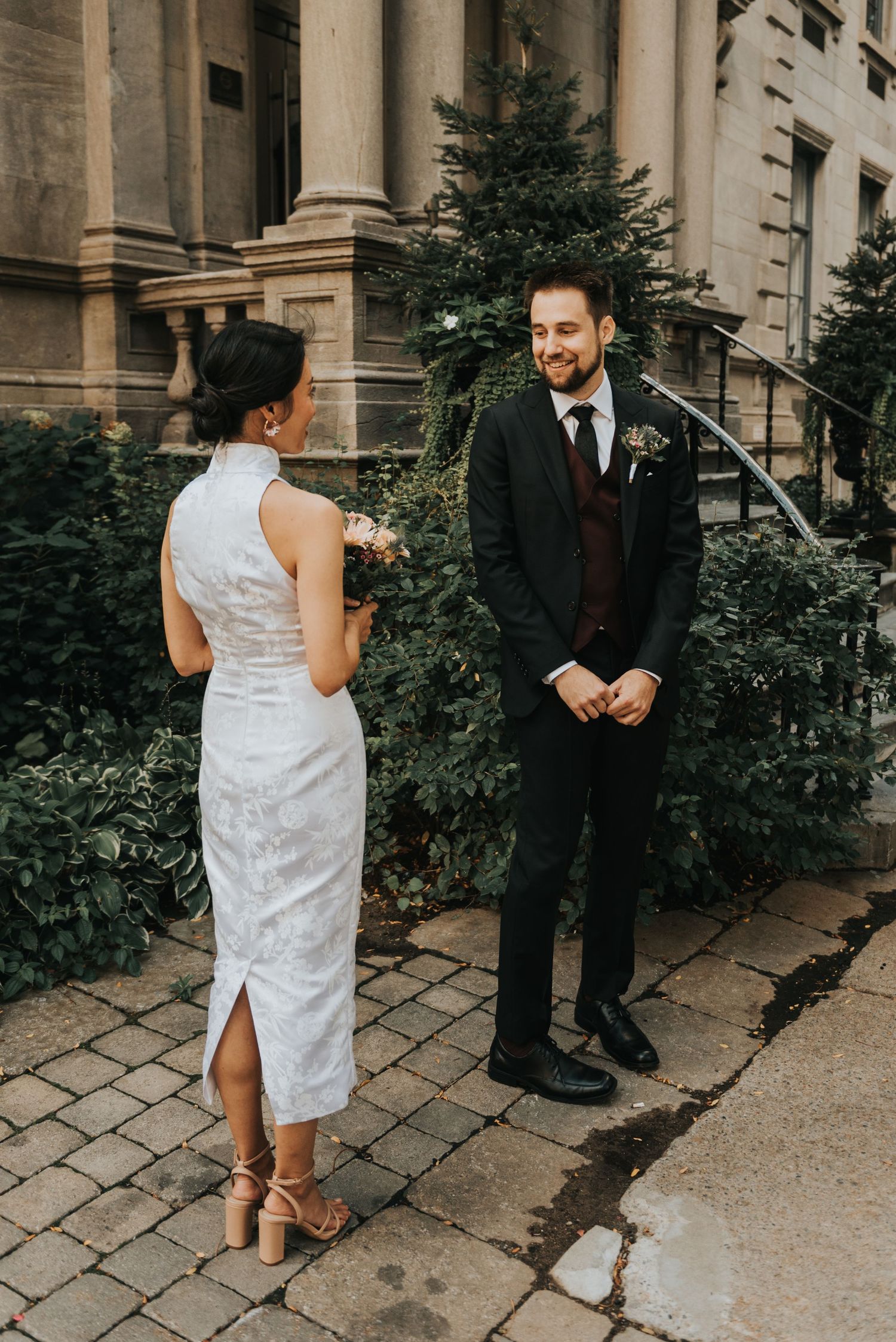 A couple shares their first look moment before their wedding outside a historic stone building with elegant columns.