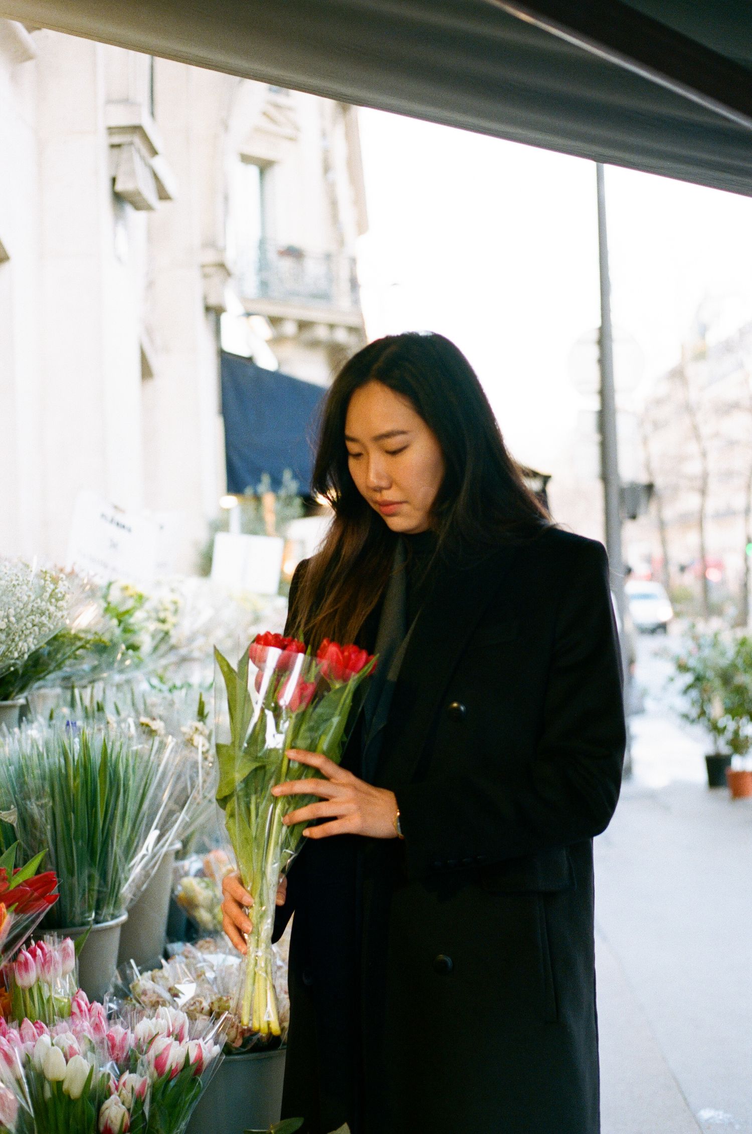 A person in a black coat browses vibrant tulips and flowers at an outdoor flower market in Paris.
