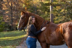 A beautiful chestnut horse stands with its handler in an autumn outdoor setting.