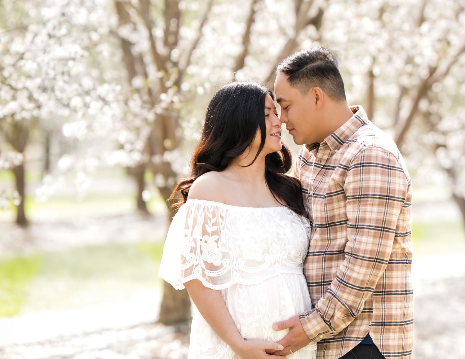 Soft sunlight filters through the cherry blossoms as a mother-to-be poses with a peaceful smile, embracing the beauty of pregnancy and natur