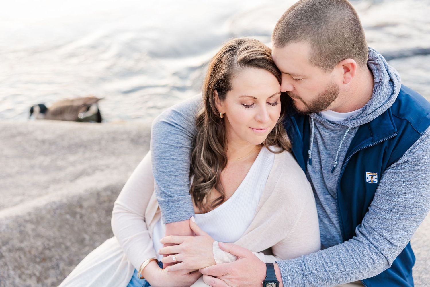 Two figures in matching grey and white clothing share an intimate moment while seated together on coastal rocks.