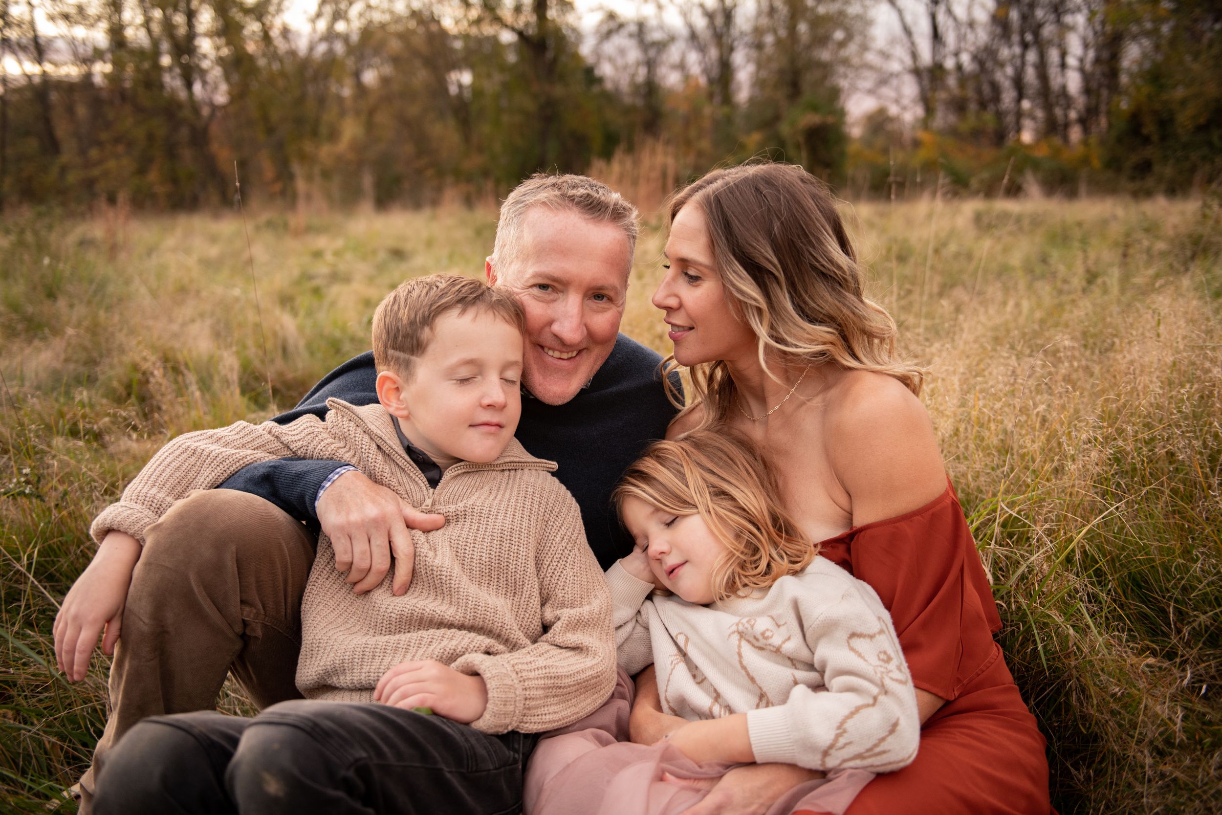 A family sits together in a golden autumn field during sunset sharing a tender moment together.