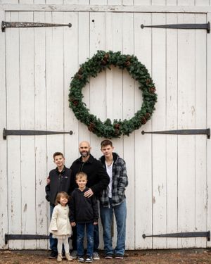Family poses in front of white barn doors with Christmas wreath decoration.