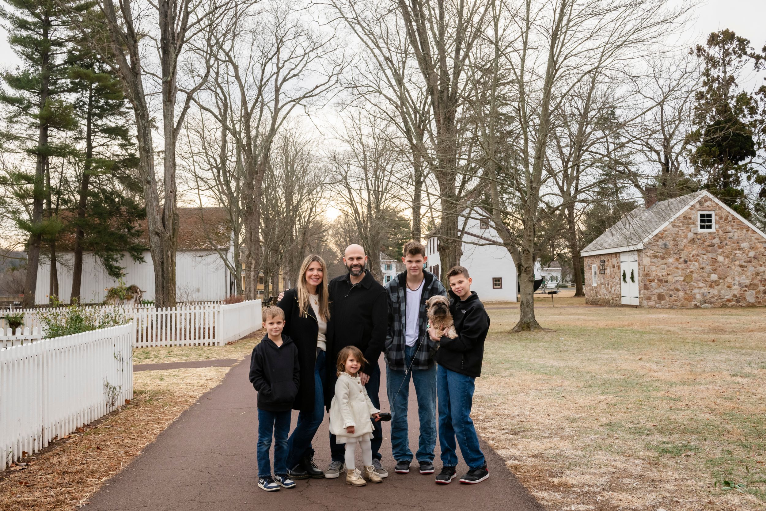 Multi-generational family group poses together on path with stone building in background.