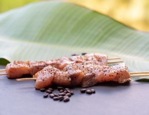 Raw meat skewers seasoned with black pepper on a banana leaf with coffee beans scattered around.