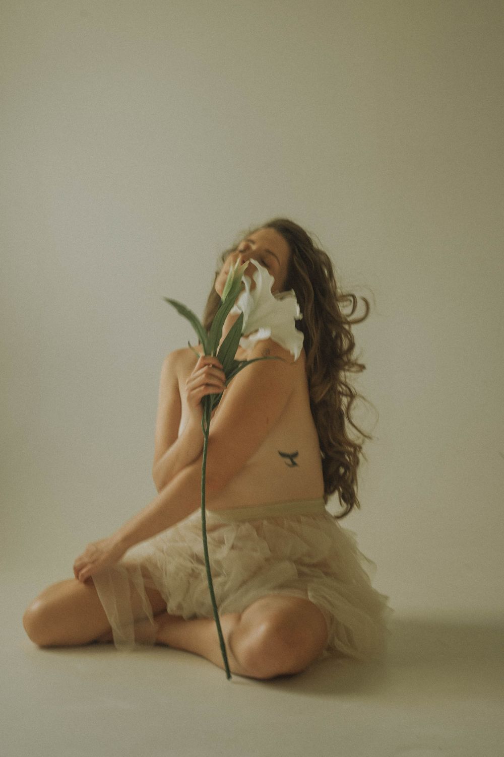 Artistic nude photography series with a white lily flower against neutral background.
