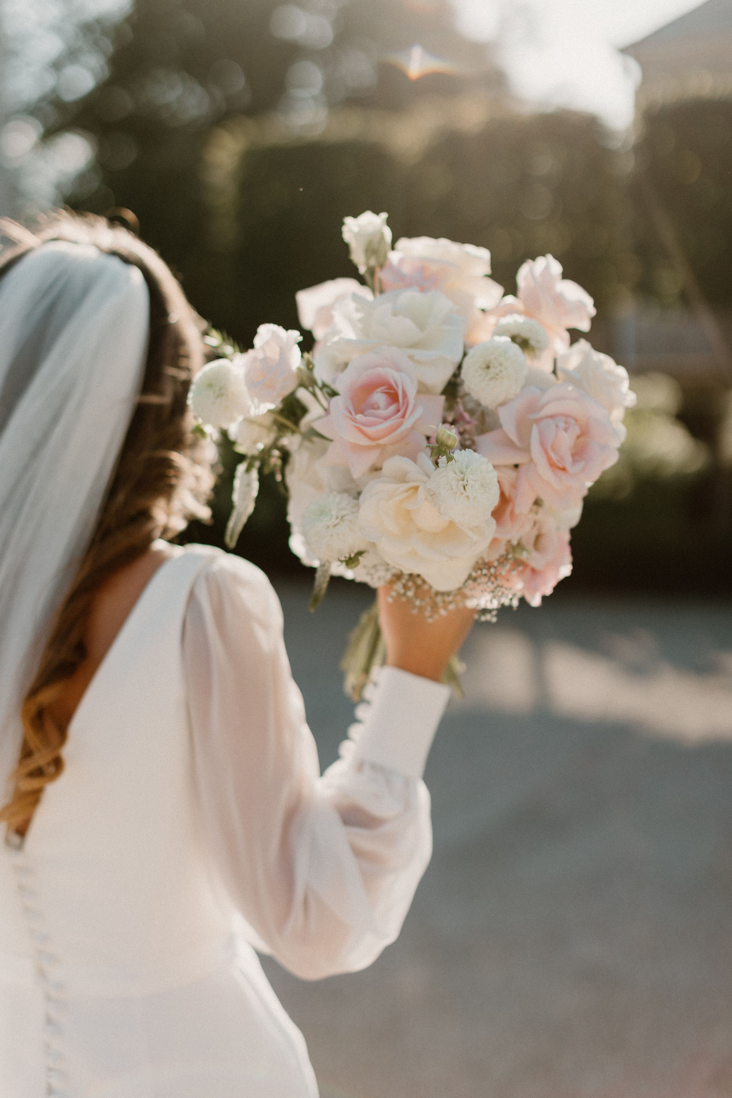 A delicate pink and white bridal bouquet held up against a sunset background.