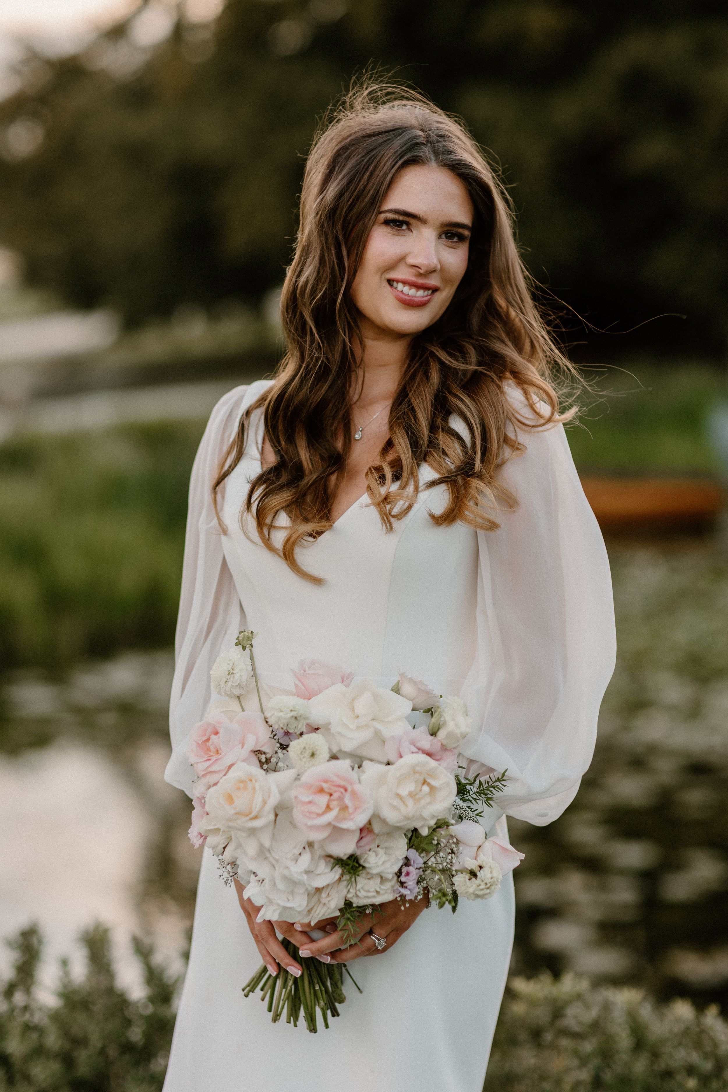 Bride in a flowing white dress with billowy sleeves holds a romantic bouquet of pink and white flowers.