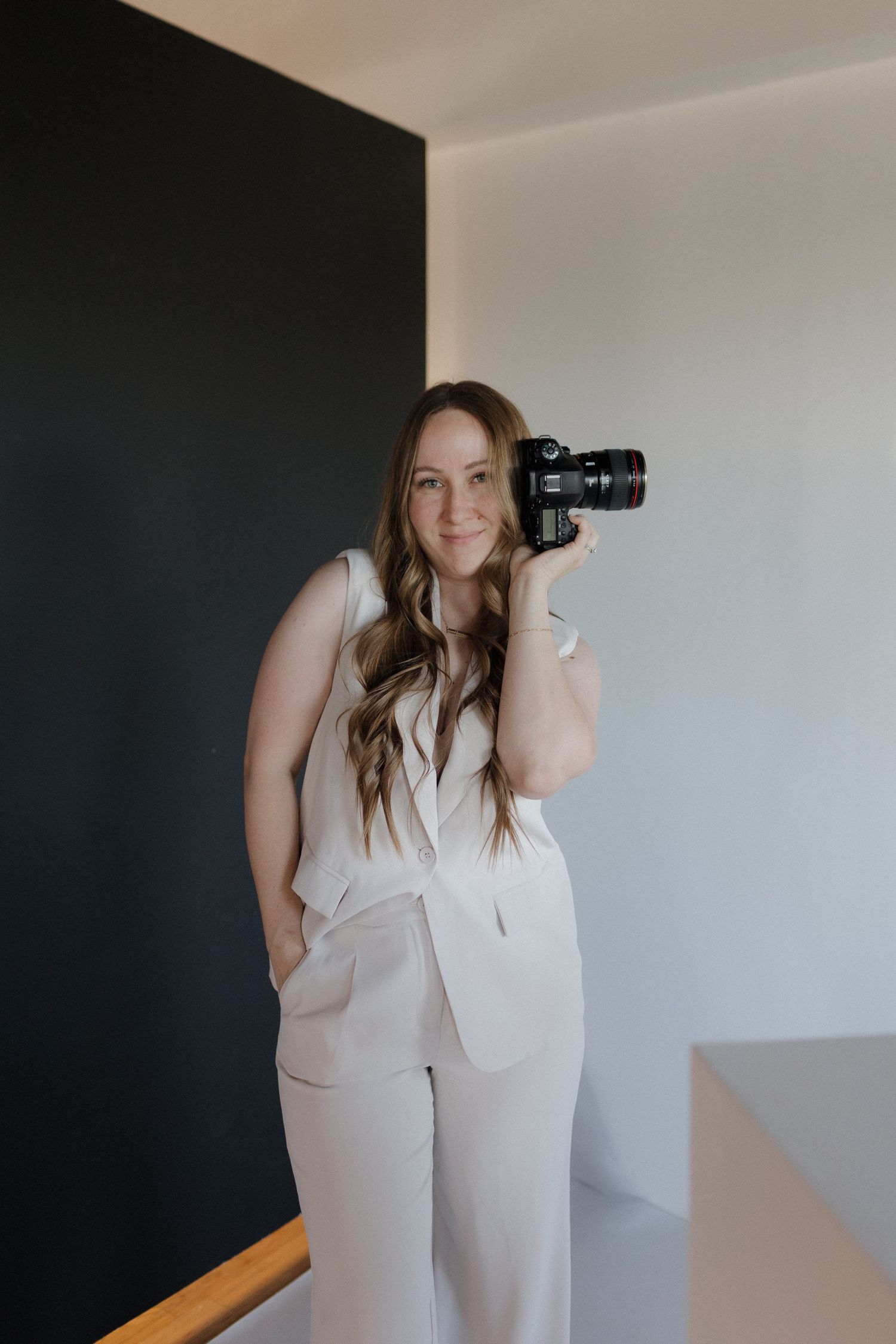 Photographer in all-white attire showcases creative poses while holding camera in bright studio setting.