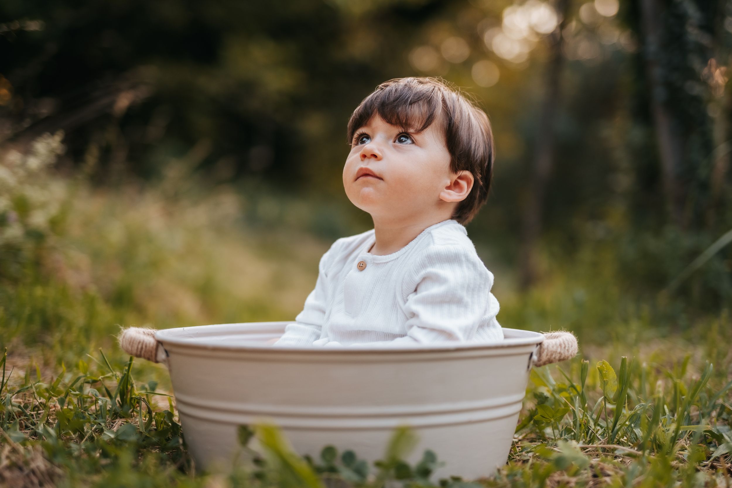 Bambino di un anno seduto in una tinozza vintage con sfondo verde della natura