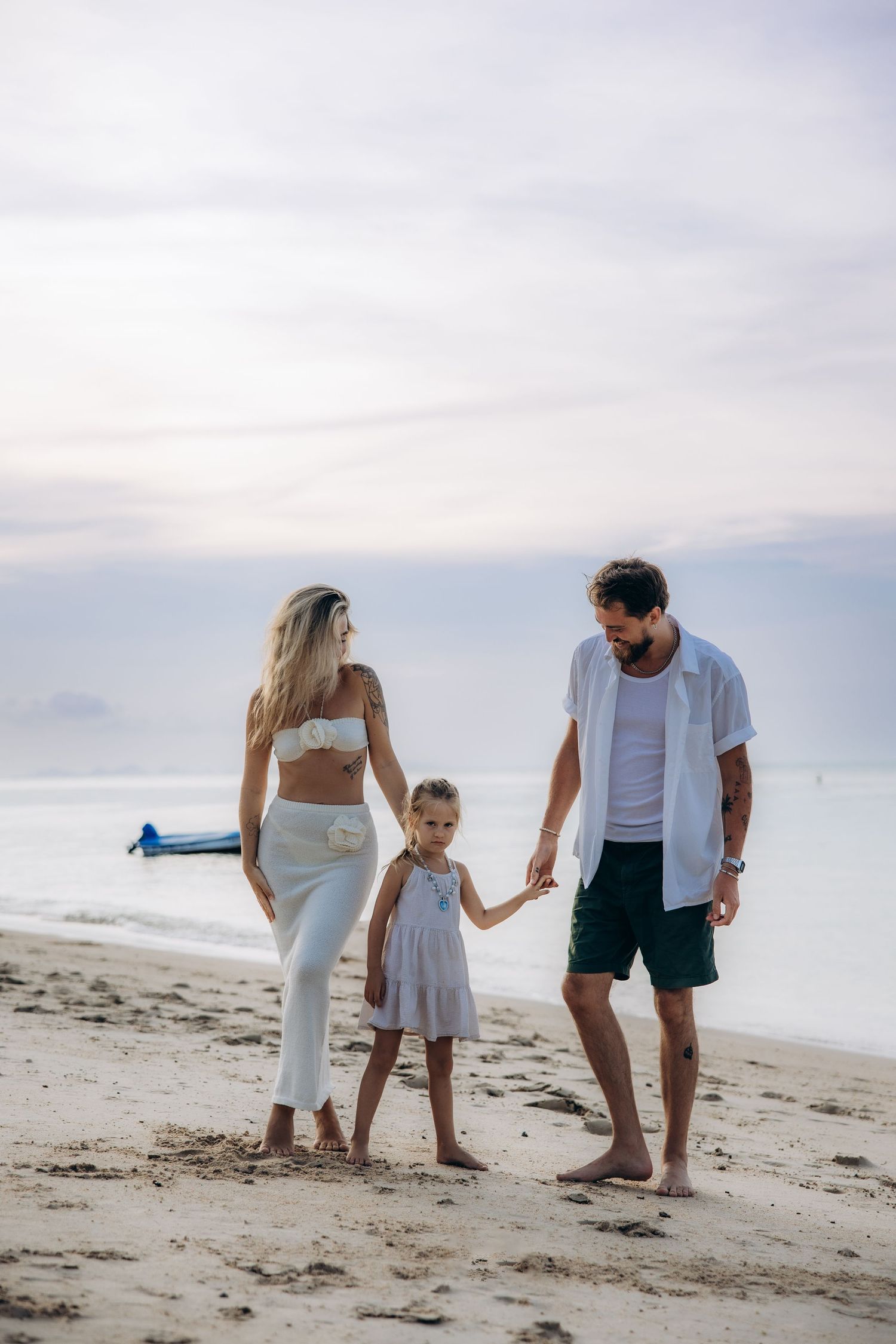 A family walks together holding hands on a sandy beach at sunset with calm ocean waters in the background.