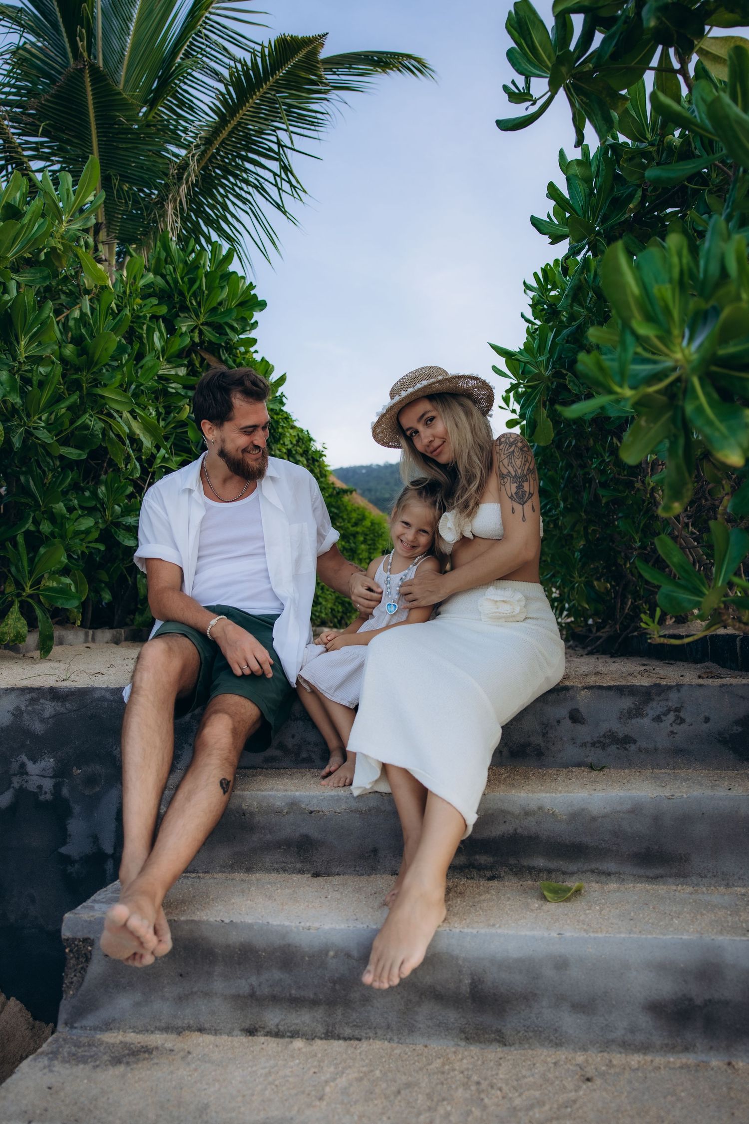 A relaxed family scene on concrete steps surrounded by lush tropical foliage and palm trees.