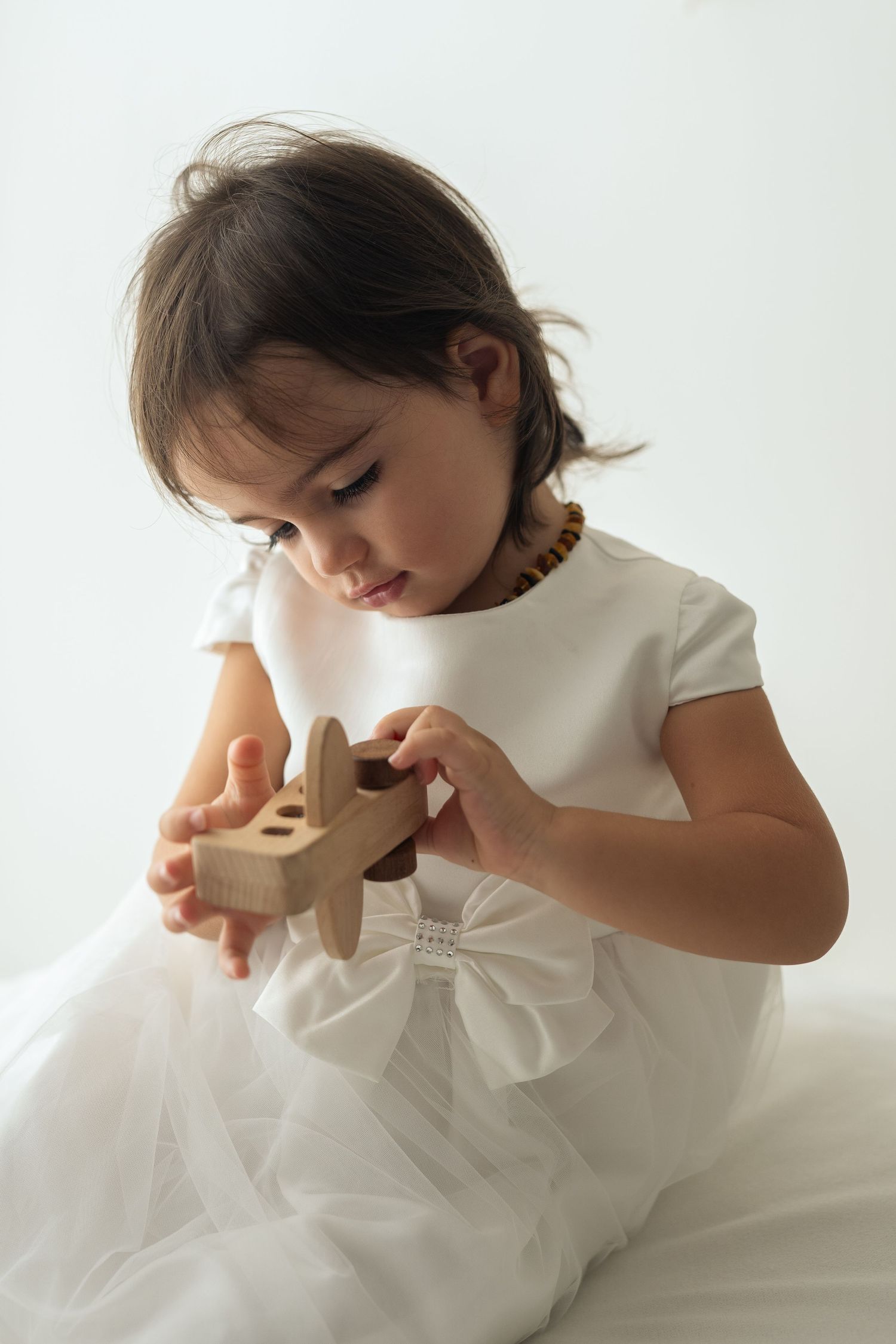 Bambina di un anno e mezzo che gioca con un aeroplanino di legno con espressione pensierosa e concentrata