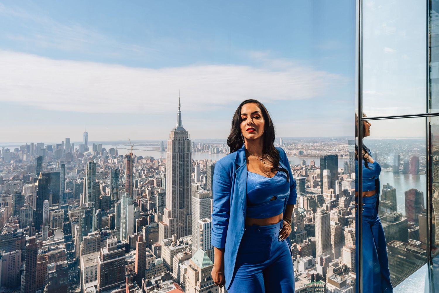 Person in blue dress admiring the New York City skyline with Empire State Building from an observation deck.