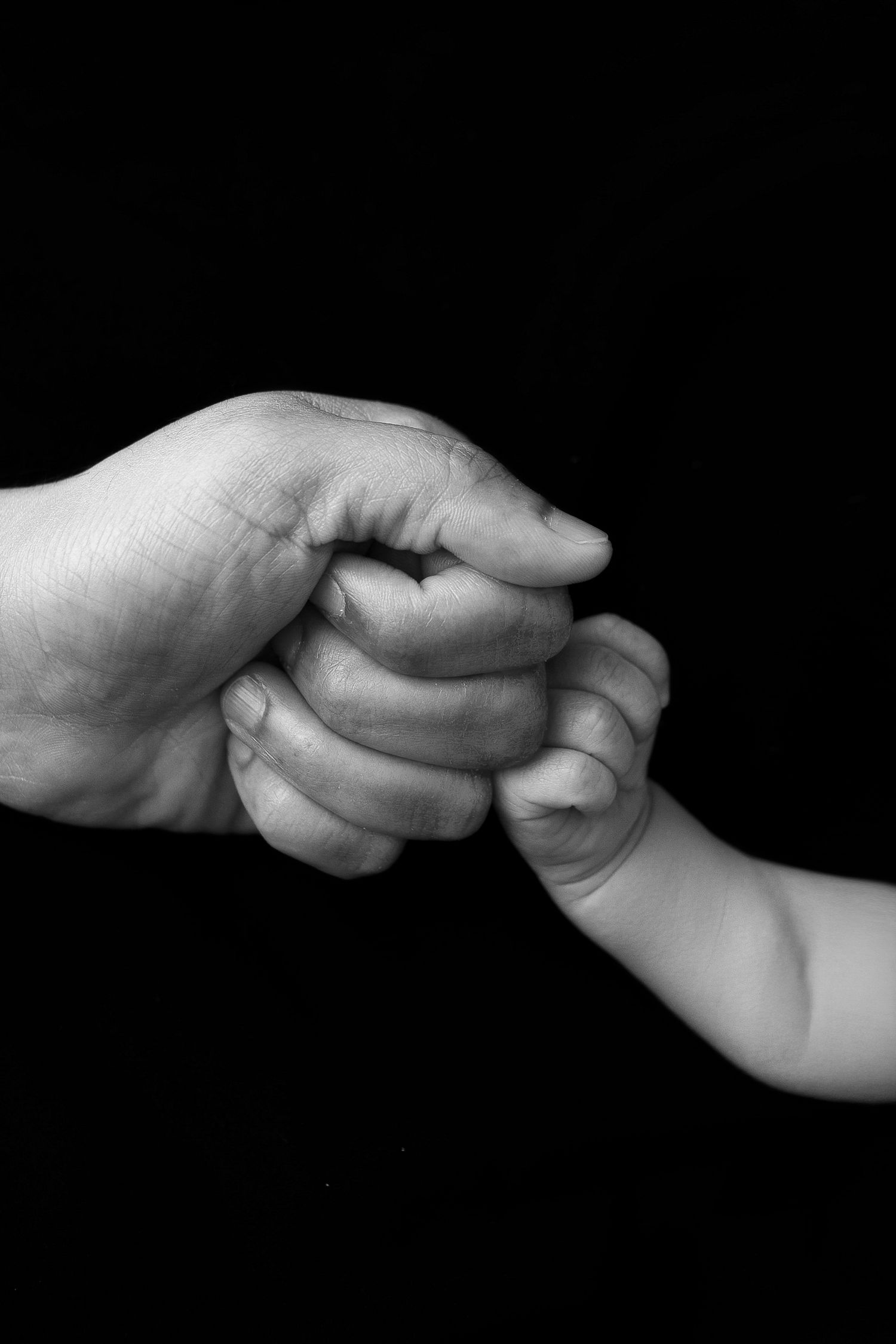 A parent in a black top cradles their sleeping newborn baby against a dark background in a tender studio portrait.