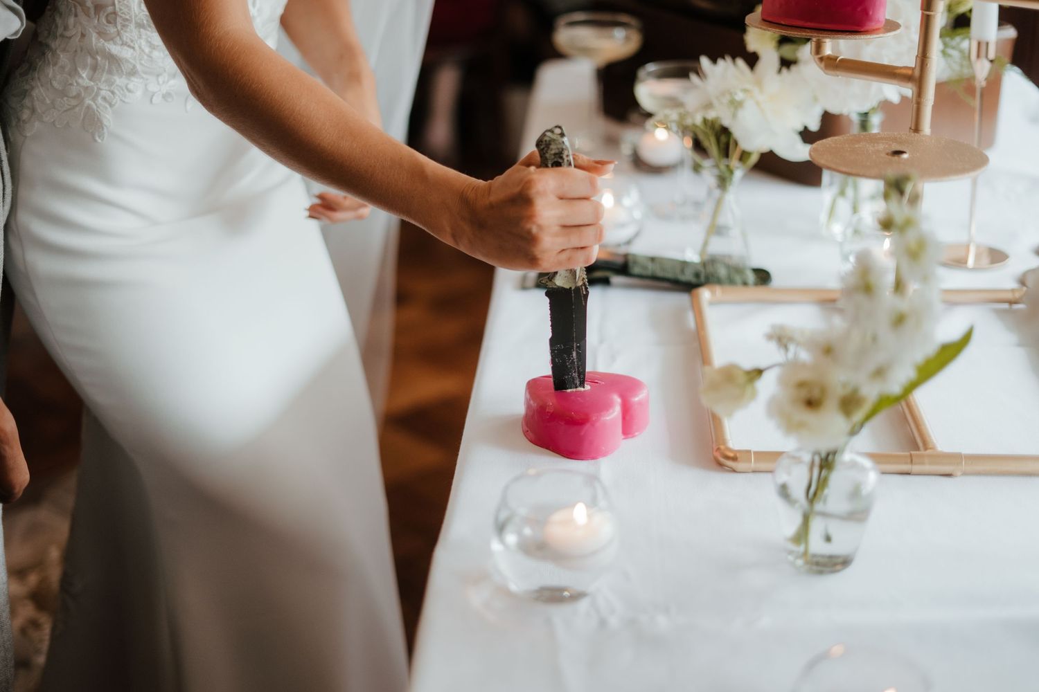 Someone in a white wedding dress pours wine at an elegant table setting with candles and floral centerpieces.