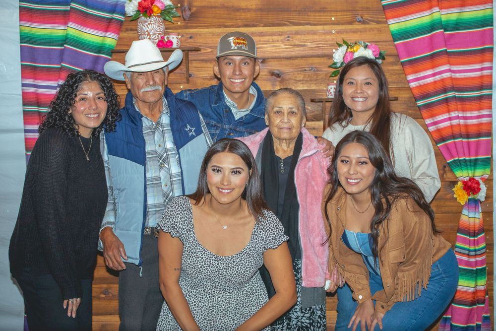 Group photo with colorful Mexican serape blankets hanging as backdrop decor.