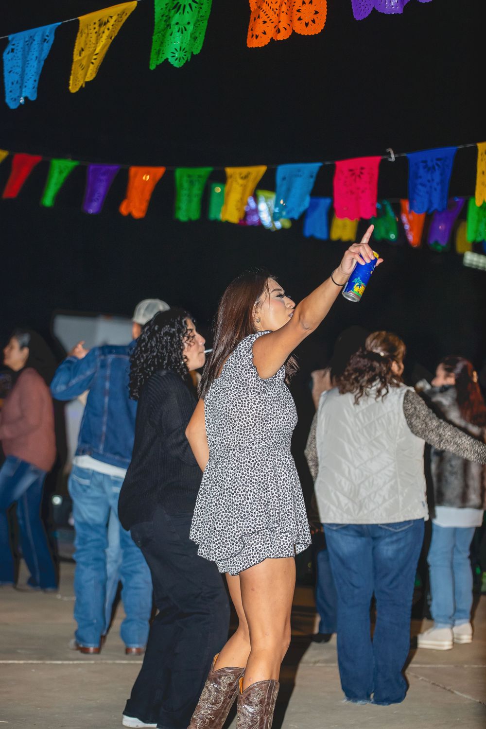 People dancing at a nighttime party under colorful papel picado banners.