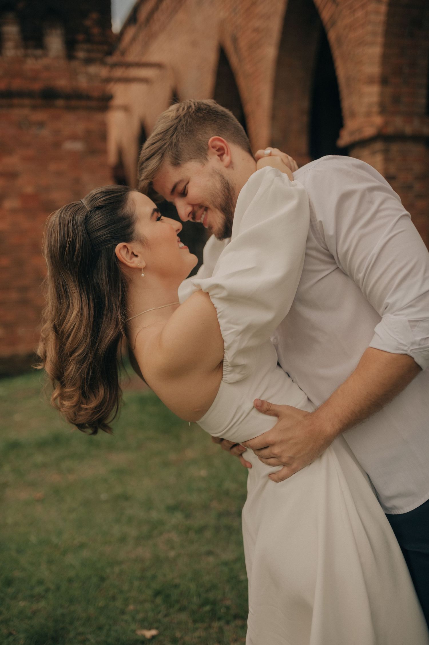 Couple in white sharing intimate moment against brick archway backdrop.