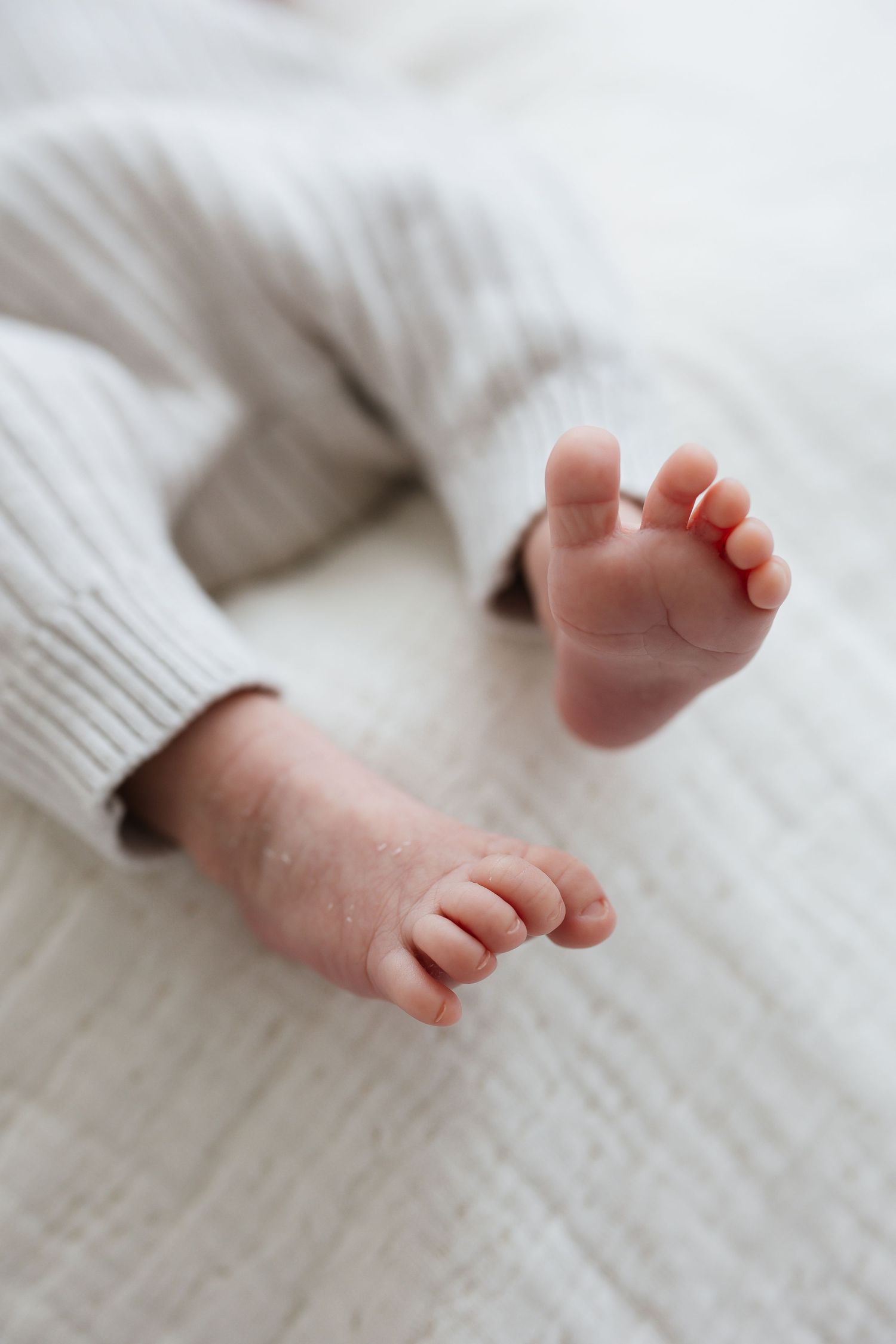 Close-up of tiny newborn baby feet in gray ribbed pants on white blanket.