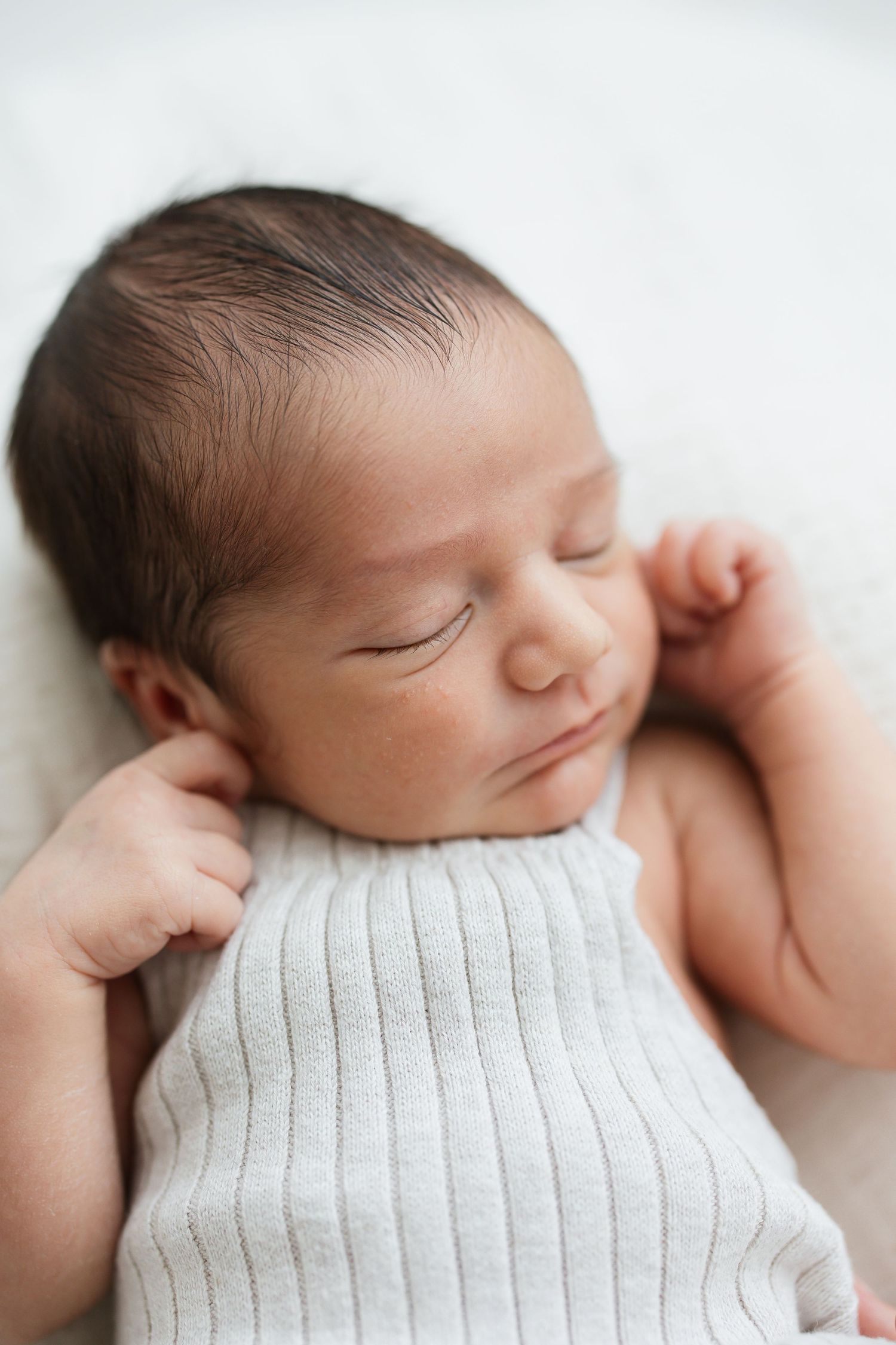 Peaceful newborn baby sleeping in a white ribbed outfit on a soft white surface.