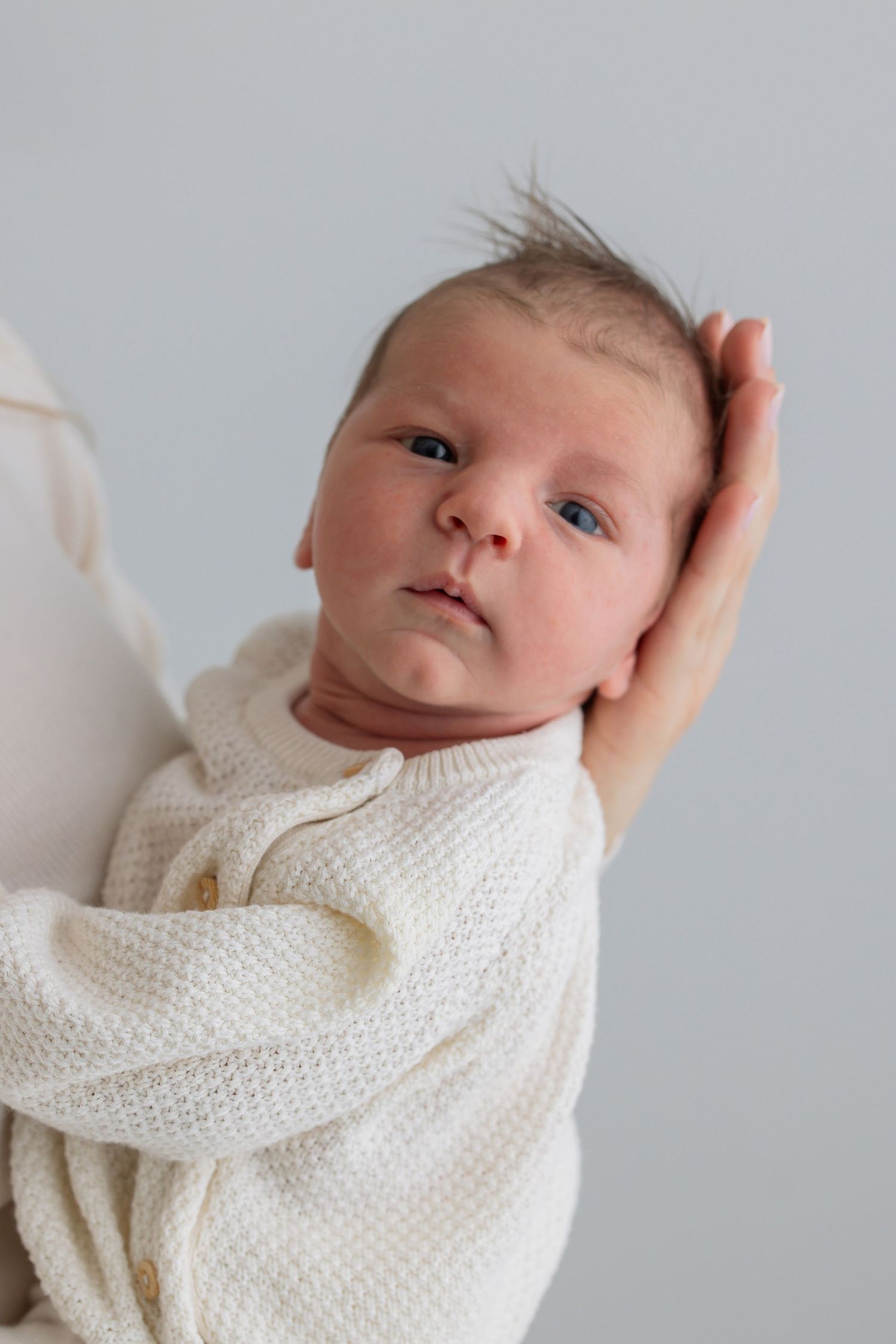 Newborn baby in cream knit sweater being held securely in parent's arms.