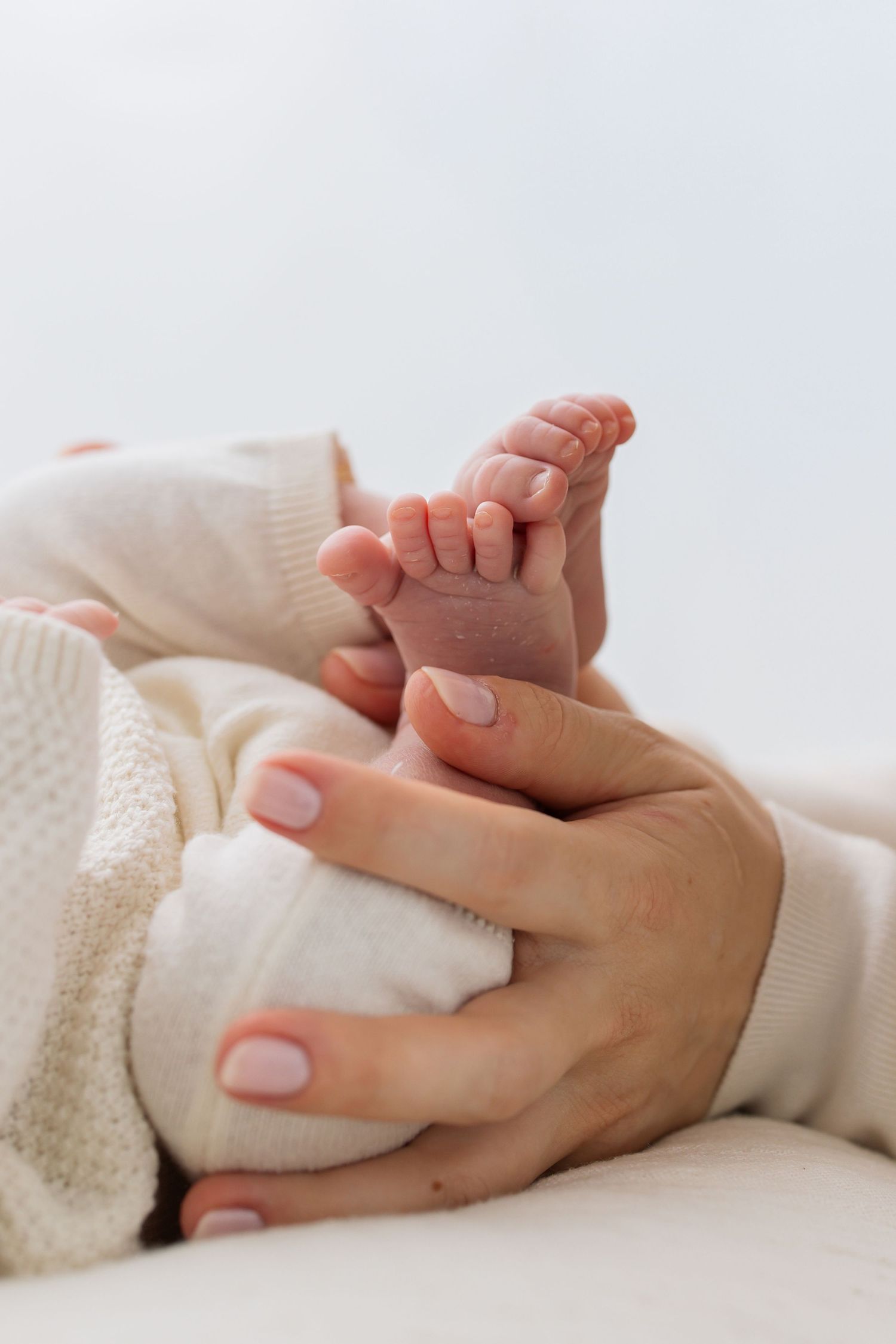 Mother's hands gently holding newborn baby's tiny feet wrapped in white blanket.