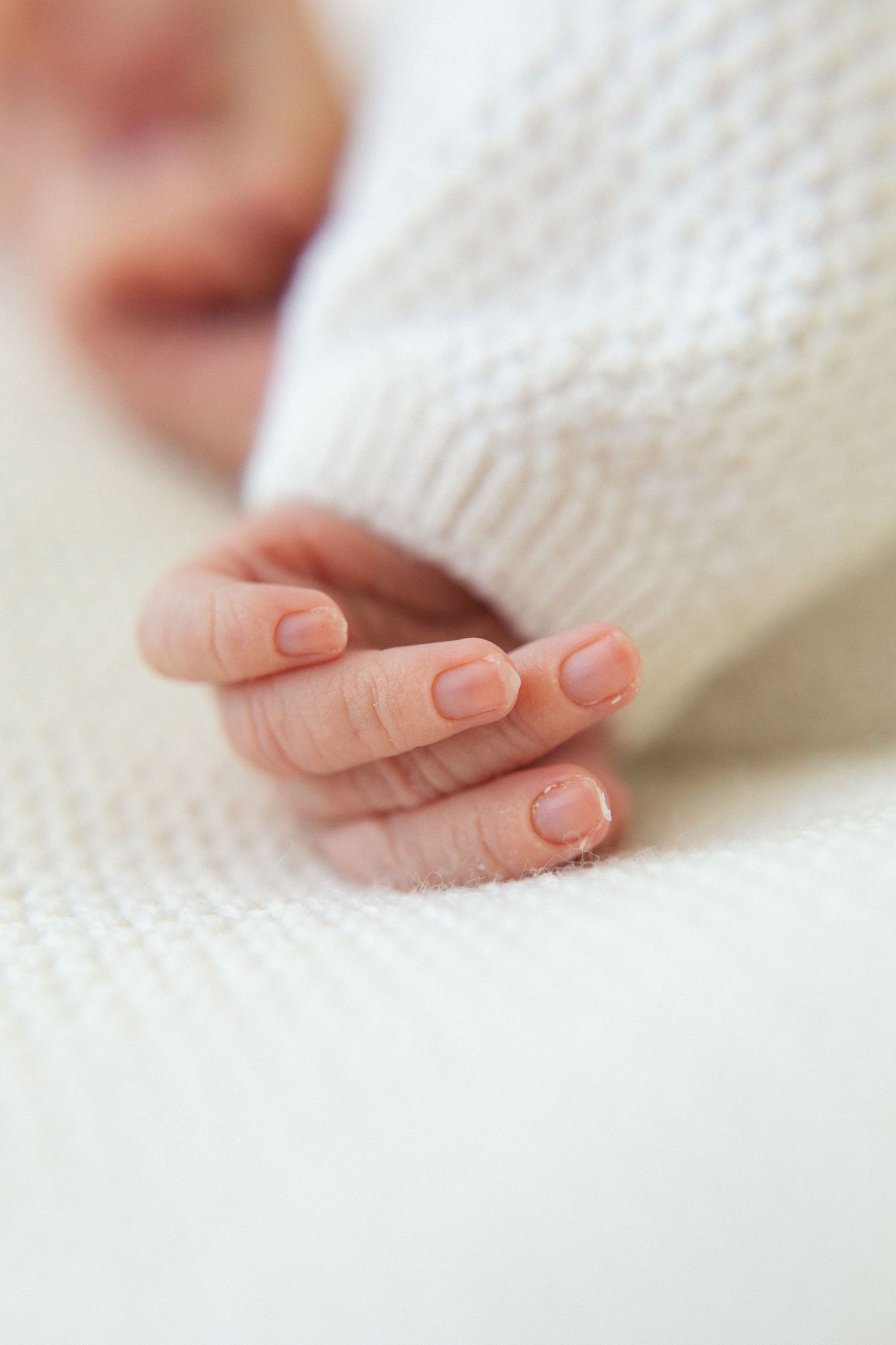 Close-up of tiny newborn baby fingers resting on white knit fabric.