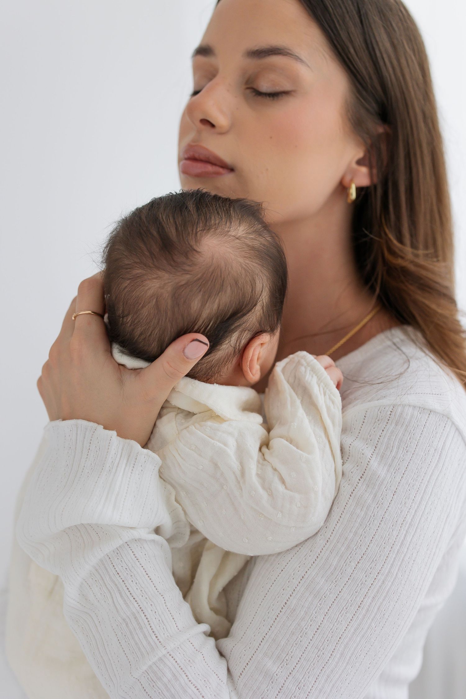 A mother tenderly holds her sleeping newborn baby against her chest with eyes closed.
