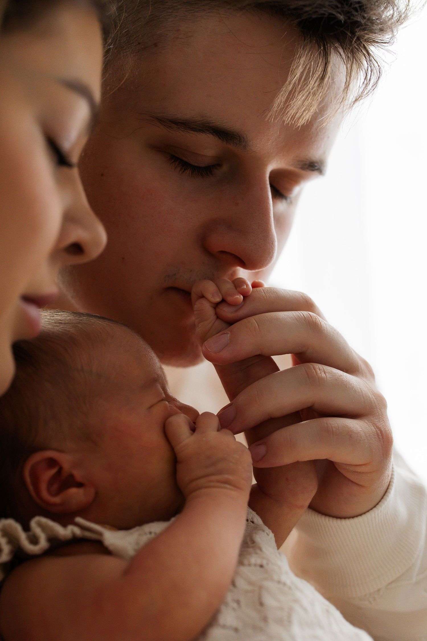 Father kissing newborn baby's tiny hand while mother holds infant close.