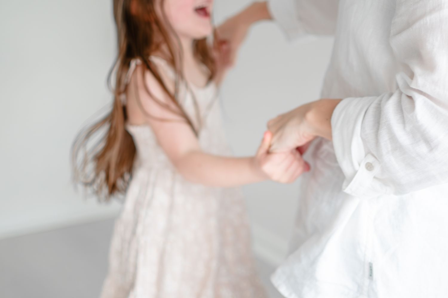 Two people in white outfits dancing together in an elegant pose against a light background.