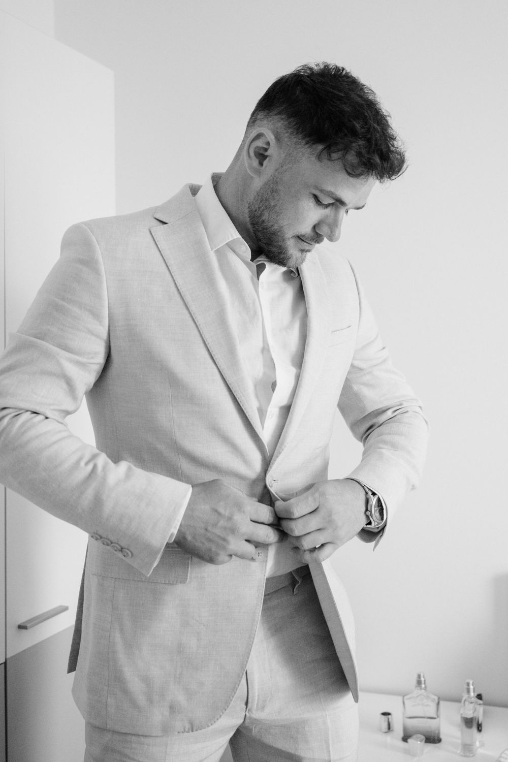 A man in a light colored suit adjusts his jacket while wearing a wristwatch in this black and white photo.