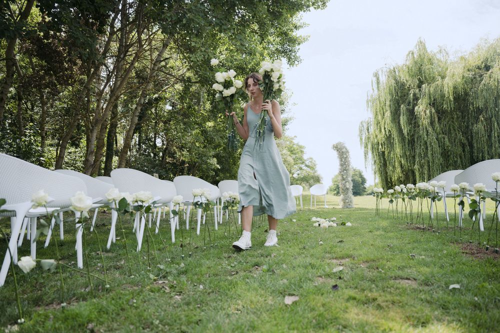 An outdoor wedding ceremony setup with white chairs on a grassy lawn bordered by tall trees and weeping willows.
