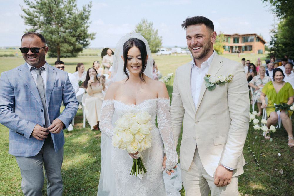 Joyful newlyweds holding hands during outdoor garden wedding ceremony with guests and minister present.