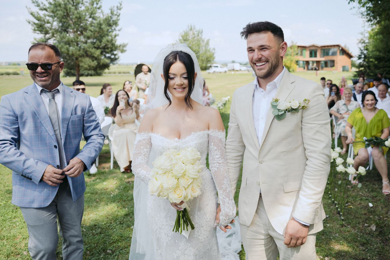 Joyful newlyweds holding hands during outdoor garden wedding ceremony with guests and minister present.